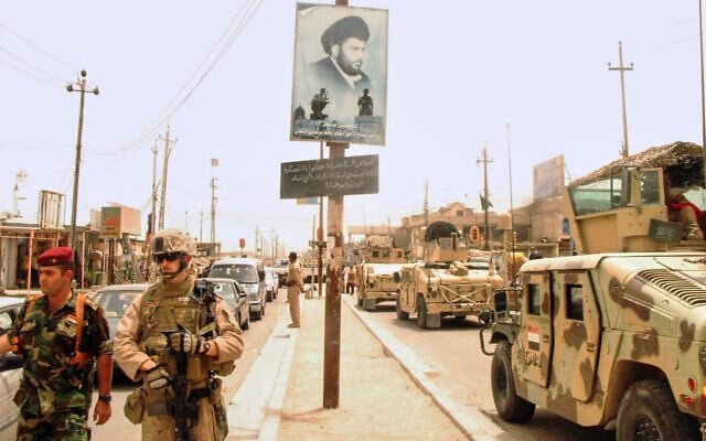 US and Iraqi troops pass a poster of Muqtada al-Sadr, evidence of continued support for the anti-American cleric and his Mahdi Army militia, in Basra, Iraq, on June 10, 2008. (AP Photo/Kim Gamel)