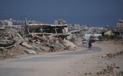 Illustrative: A Palestinian man rides his bicycle by the rubble of buildings that were destroyed during the Israel Hamas war, in southern Gaza Strip, July 31, 2026. (AP/Abdel Kareem Hana)