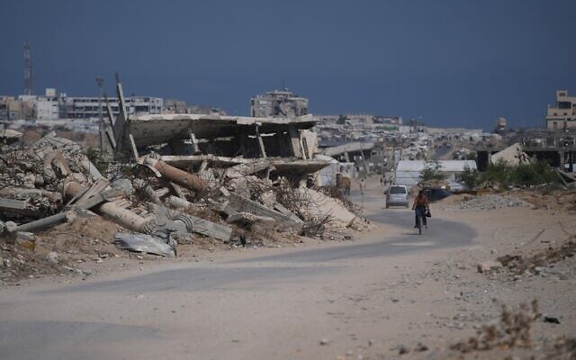 Illustrative: A Palestinian man rides his bicycle by the rubble of buildings that were destroyed during the Israel Hamas war, in southern Gaza Strip, July 31, 2026. (AP/Abdel Kareem Hana)