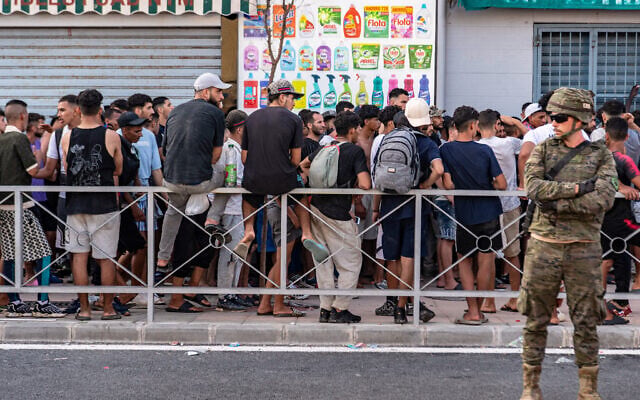 Migrants wait for a shop to open so they can buy food after crossing from Morocco into the Spanish enclave of Ceuta, July 31, 2026. (AP Photo/Antonio Sempere)