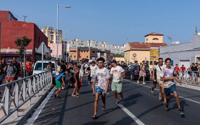 Migrants run from Spanish police officers after crossing from Morocco into the Spanish enclave of Ceuta, July 31, 2026. (AP Photo/Antonio Sempere)