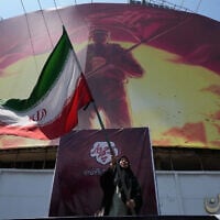 A woman waves an Iranian flag next to a billboard showing a graphic of a man wearing a shirt showing the face of late Iranian supreme leader Ayatollah Ali Khamenei with words calling upon the avengers of Imam Hussein, in a square in downtown Tehran, Iran, August 1, 2026. (AP Photo/Vahid Salemi)