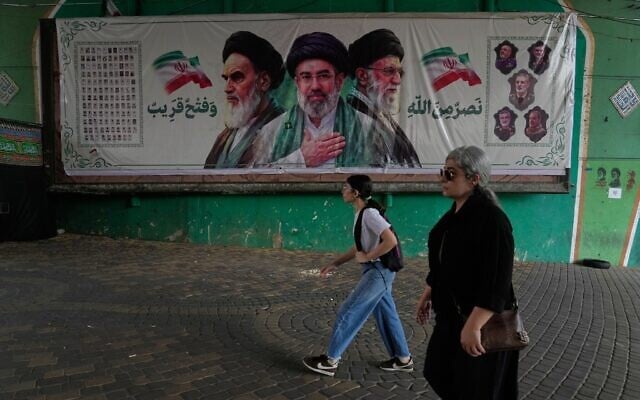 Women walk past a banner showing portraits of the late Iranian revolutionary founder Ayatollah Khomeini, left, Supreme Leader Ayatollah Mojtaba Khamenei, center, and the late supreme leader Ayatollah Ali Khamenei, who was killed in the US and Israel strike on February 28, under a bridge in northern Tehran, Iran, August 2, 2026. (AP Photo/Vahid Salemi)