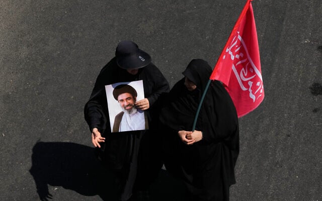 An Iranian woman carries a poster of Supreme Leader Mojtaba Khamenei as another carries a flag with words calling upon the avengers of slain supreme leader Ali Khamenei, as they attend Arbaeen religious rituals in Tehran, Iran, August 4, 2026. (AP Photo/Vahid Salemi)
