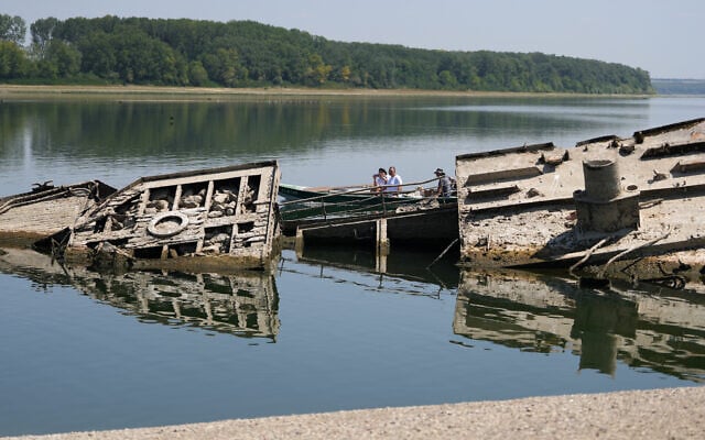People watch the wreckage of a WWII German warship, emerged due to the drought, in front of Djerdap II, a large dam on the Danube River, between Romania and Serbia, near Prahovo, Serbia, August 4, 2026. (AP Photo/Darko Vojinovic)