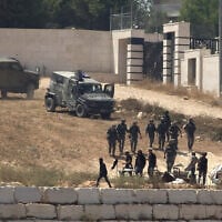 Israeli soldiers stand guard next to settlers in front of Palestinian homes that they have blockaded in the village of Qusra, south of Nablus, in the West Bank, August 12, 2026. (AP Photo/Nidal Eshtayeh)