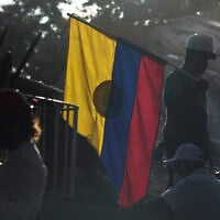 A firefighter working on rescue efforts holds a Colombian flag amid the rubble three days after an earthquake struck Cali, Colombia, August 13, 2026. (AP Photo/Ivan Valencia)
