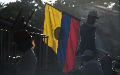 A firefighter working on rescue efforts holds a Colombian flag amid the rubble three days after an earthquake struck Cali, Colombia, August 13, 2026. (AP Photo/Ivan Valencia)