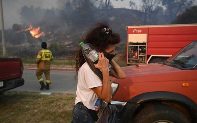 Illustrative: A woman covers her face to protect herself from smoke during a wildfire in Siviri, on the Chalkidiki peninsula in northern Greece, August 13, 2026. (AP/Giannis Papanikos)