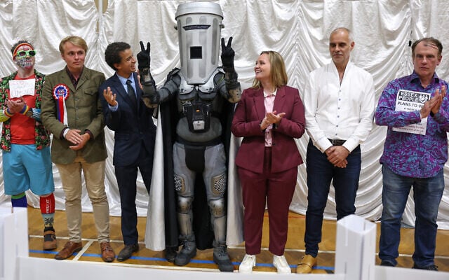 Count Binface, center, stands among other candidates during the result announcement after the Clacton by-election count at the Leisure Centre in Clacton on Sea, England, August 14, 2026. (AP Photo/Richard Pelham)