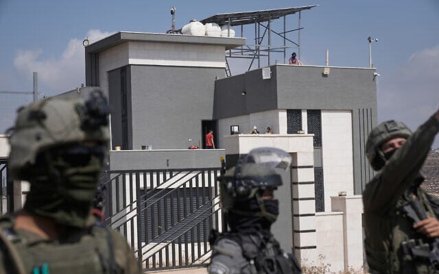 Israeli forces stand in front of the entrance of a Palestinian house besieged by Israeli settlers in the village of Qusra, south of Nablus, in the West Bank, on August 14, 2026. (AP Photo/Majdi Mohammed)