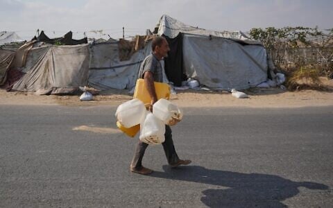 A displaced Palestinian man carries empty containers while heading to refill fresh water in Deir al-Balah, central Gaza Strip, Friday, Aug 14, 2026. (AP/Abdel Kareem Hana)