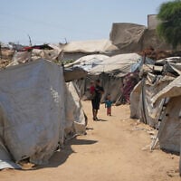 A displaced Palestinian man walks with his children at a camp in Deir al-Balah, central Gaza Strip, Augist 14, 2026. (AP Photo/Abdel Kareem Hana)