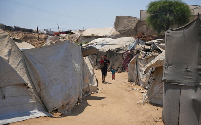 A displaced Palestinian man walks with his children at a camp in Deir al-Balah, central Gaza Strip, Augist 14, 2026. (AP Photo/Abdel Kareem Hana)