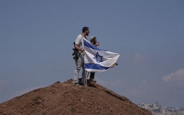 Israeli settlers put up an Israeli flag on a hilltop after it was taken down by Israeli and foreign peace activists during a protest in support of local landowners whose property is threatened with seizure by settlers, on the outskirts of the West Bank city of Beit Sahour, August 14, 2026. (AP Photo/Mahmoud Illean)