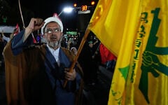 A cleric in Iran chants a slogan as he holds a flag of Lebanon’s Hezbollah during a pro-government gathering in Tehran, August 26, 2026. (AP Photo/Vahid Salemi)