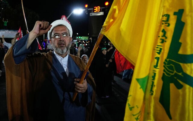 A cleric in Iran chants a slogan as he holds a flag of Lebanon’s Hezbollah during a pro-government gathering in Tehran, August 26, 2026. (AP Photo/Vahid Salemi)