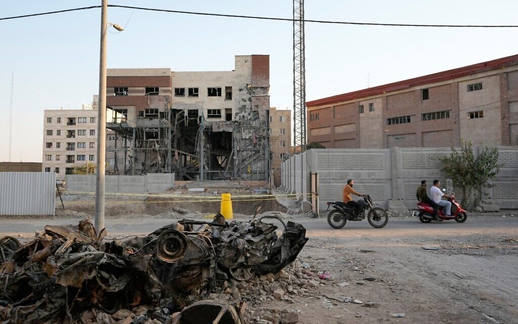 Men on motorbikes drive past cars and a residential building damaged in a March 8 US-Israeli strike in Tehran, Iran, August 27, 2026. (AP/Vahid Salemi)