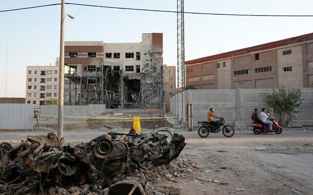 Men on motorbikes drive past cars and a residential building damaged in a March 8 US-Israeli strike in Tehran, Iran, August 27, 2026. (AP/Vahid Salemi)