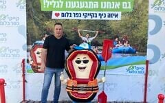 Eyal Greenwald, marketing manager of Kfar Blum Kayaks, stands in front of a sign that reads, 'We also missed the Galilee!' on Kibbutz Kfar Blum, in the Upper Galilee, on August 11, 2026. (Diana Bletter/Times of Israel)