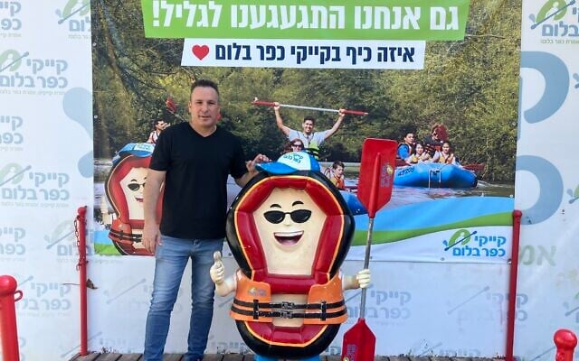Eyal Greenwald, marketing manager of Kfar Blum Kayaks, stands in front of a sign that reads, 'We also missed the Galilee!' on Kibbutz Kfar Blum, in the Upper Galilee, on August 11, 2026. (Diana Bletter/Times of Israel)