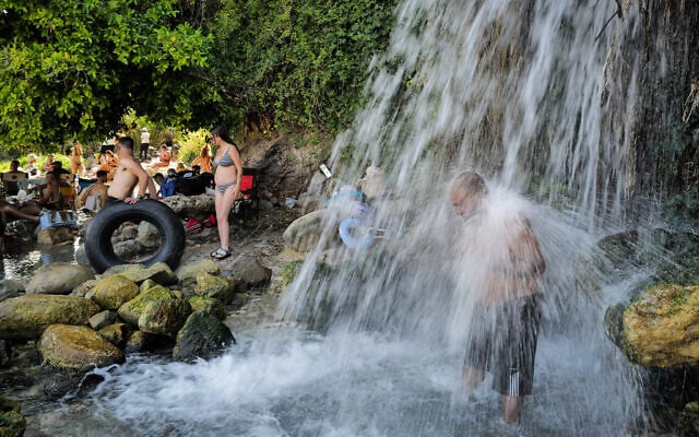 People enjoy a waterfall flowing into the Sea of Galilee near Kfar Nahum, northern Israel, August 1, 2026. (Michael Giladi/Flash90)