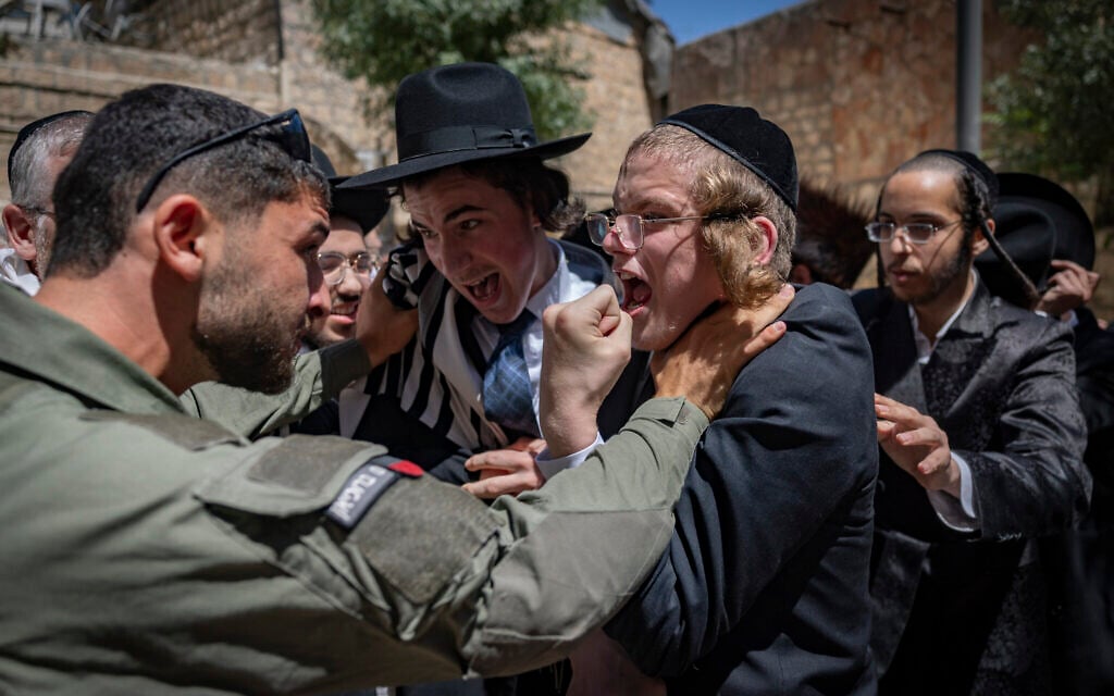 A police officer clutches the neck of an ultra-Orthodox youth during a Haredi riot outside a cafe operating on Shabbat, in Jerusalem, August 1, 2026. (Yonatan Sindel/Flash90)