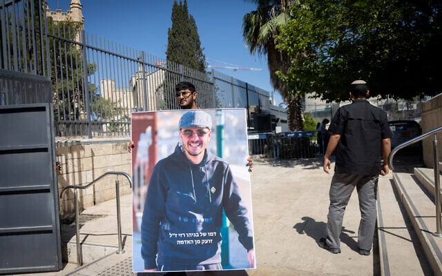 A young man holds an picture of Benayahu Razi who was murdered last month in Jerusalem, outside a court hearing on August 7, 2026. (Chaim Goldberg/FLASH90)