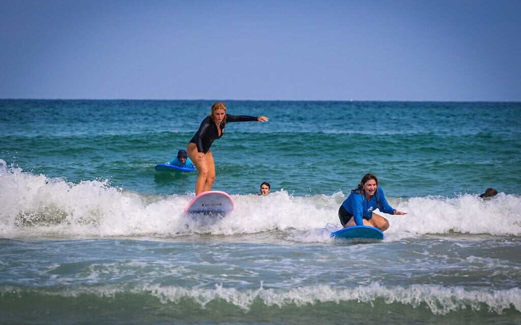 People surf off the coast in Tel Aviv, August 8, 2026. (Avshalom Sassoni/Flash90)