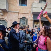 Haredi men protest outside the Basimta cafe for opening on Shabbat while secular counterprotesters stand in front of them, in Jerusalem on August 8, 2026. (Oren Ben Hakoon/Flash90)