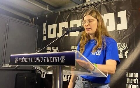Shir Matias, whose parents Deborah (Shachar) and Shlomi were killed protecting her brother Rotem at their Kibbutz Holit home in the Hamas-led onslaught of October 7, 2023, speaks at an anti-government rally in Habima Aquare, Tel Aviv, August 1, 2026. (Movement for Quality Government in Israel)