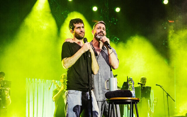 Former hostage Sagui Dekel-Chen and HaTivka6 lead singer Omri Glickman as they perform a song Dekel-Chen composed in captivity in a show on the lawn of Kibbutz Nir Oz as part of the Israel Festival on August 10, 2026 (Orit Pnini)