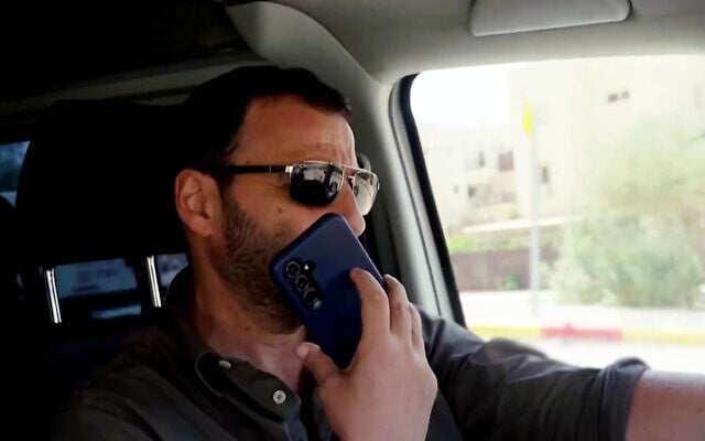 Channel 13 reporter Raviv Drucker seen driving with one hand on the steering wheel and the other hand holding a phone, in a segment that aired on September 23, 2026. (Screenshot/Channel 13)