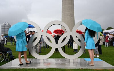 Hostesses and visitors stand next to Olympic Rings that were installed on the roof of the small Olympic Hall to mark the 50th anniversary of the 1972 Summer Olympics in Munich on July 1, 2022. (Christof STACHE/AFP)