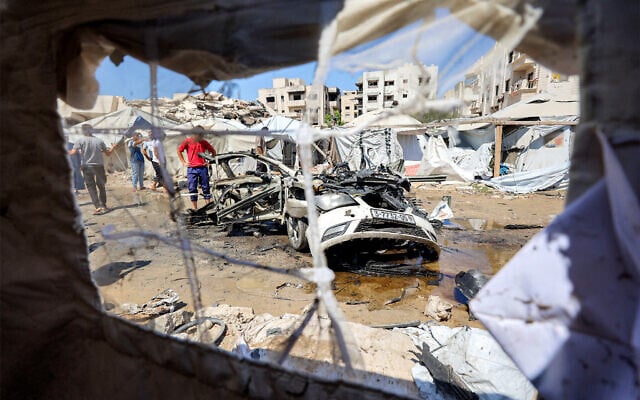 People gather around a destroyed vehicle following an Israeli strike in the Rimal neighborhood of Gaza City on September 1, 2026. (Omar AL-QATTAA/AFP)