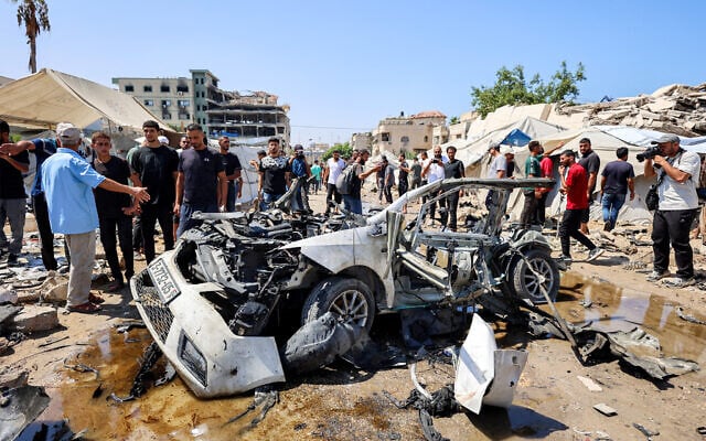 People gather around a destroyed vehicle following an Israeli strike in the Rimal neighborhood of Gaza City on September 1, 2026. (Omar AL-QATTAA/AFP)