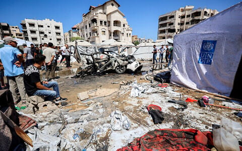 People gather near a destroyed vehicle following an Israeli strike in the Rimal neighborhood of Gaza City on September 1, 2026. (Omar AL-QATTAA/AFP)