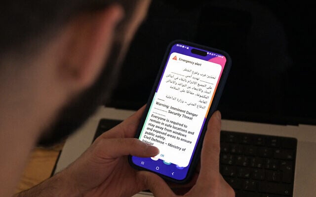A Kuwaiti man holds his mobile phone displaying an alert message as sirens sound during an Iranian missile or drone attack, in Kuwait City early on September 2, 2026. (AFP)