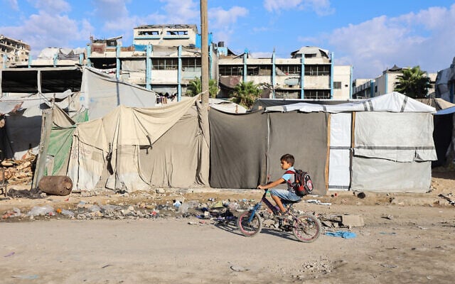 Illustrative: A Palestinian boy rides his bike past makeshift shelters on his way to school as the academic year begins in Gaza City, in the Strip's north, on September 19, 2026. (Omar AL-QATTAA/AFP)