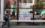 A woman walks by signs hanging in a window inside of a school building at the University of Antwerp, as pro-Palestinian students occupy parts of the campus in Antwerp, Belgium, May 14, 2024. (AP/Virginia Mayo)