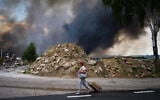A woman walks along a road as smoke rises from a destroyed warehouse after a Russian drone attack on the outskirts of Kyiv, Ukraine, August 27, 2026. (AP Photo/Francisco Seco)