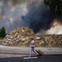 A woman walks along a road as smoke rises from a destroyed warehouse after a Russian drone attack on the outskirts of Kyiv, Ukraine, August 27, 2026. (AP Photo/Francisco Seco)