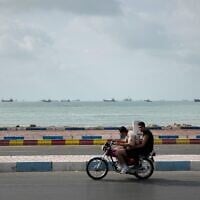 Two men ride a motorcycle along the waterfront as commercial vessels lie anchored in the Strait of Hormuz off Bandar Abbas, Iran, September 4, 2026. (AP Photo/Vahid Salemi)