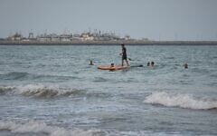 A man paddleboards among swimmers in the Strait of Hormuz, with boats docked at a harbor in Bandar Abbas, Iran, September 4, 2026. (AP Photo/Vahid Salemi)