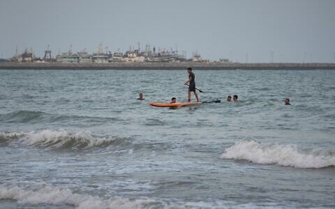 A man paddleboards among swimmers in the Strait of Hormuz, with boats docked at a harbor in Bandar Abbas, Iran, September 4, 2026. (AP Photo/Vahid Salemi)