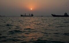 The sun sets over commercial vessels anchored in the Strait of Hormuz off Bandar Abbas, Iran, with the city’s skyline in the background, September 6, 2026. (AP Photo/Vahid Salemi)