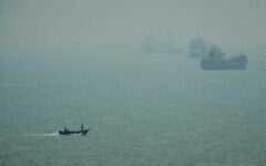 A motorboat travels past commercial vessels anchored amid haze in the Strait of Hormuz off Bandar Abbas, Iran, September 7, 2026. (AP Photo/Vahid Salemi)