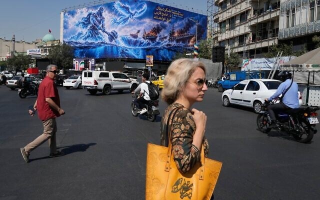 Pedestrians walk past a billboard depicting a Persian legendary hero and flying figure hitting US aircraft carriers alongside the message in English and Farsi: 'From the Persian Gulf a new power rises' and 'The army of Satan will be drowned in the Persian Gulf,' at Islamic Revolution square in downtown Tehran, Iran, September 14, 2026. (AP Photo/Vahid Salemi)