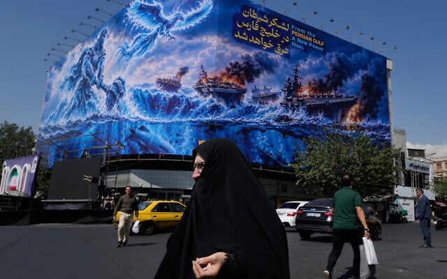 Pedestrian walk past a billboard depicting a Persian legendary hero and flying figure hitting US aircraft carriers alongside the message in English and Farsi: 'From the Persian Gulf a new power rises. The army of Satan will be drowned in the Persian Gulf,' at Islamic Revolution square in downtown Tehran, Iran, September 14, 2026. (AP Photo/Vahid Salemi)