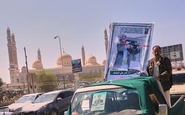 A man stands beside a portrait of Houthi fighter Mohammed Omar Ali al-Saqqaf, also known as Abu Fatima, mounted on a pickup truck during a mass funeral procession, with Al-Saleh Mosque in the background, in Sanaa, Yemen, September 16, 2026. (AP Photo)